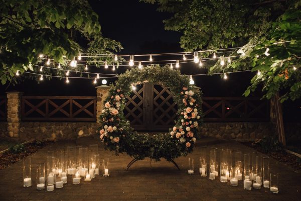 beautiful-photozone-with-big-wreath-decorated-with-greenery-roses-centerpiece-candles-sides-garland-hanged-trees-min